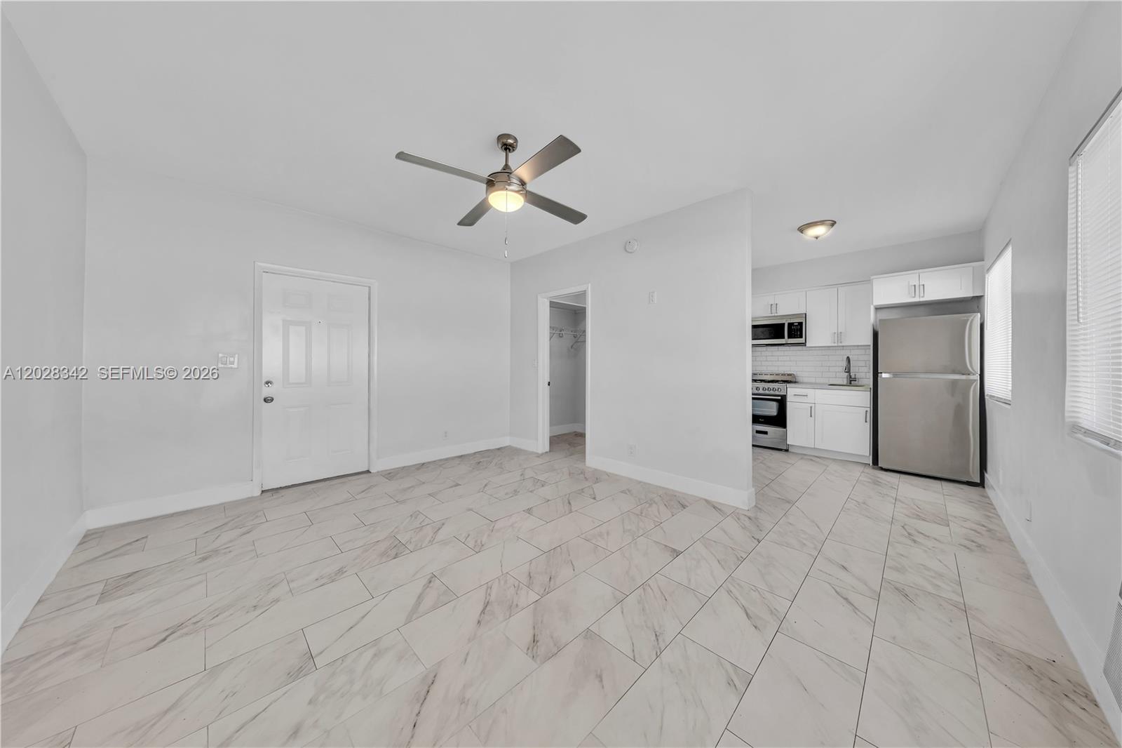 A room with white walls, marble-look tile flooring, a ceiling fan, and an adjacent kitchen — 1839 Funston St # 4, Hollywood FL 33020, HOLLYWOOD, FL