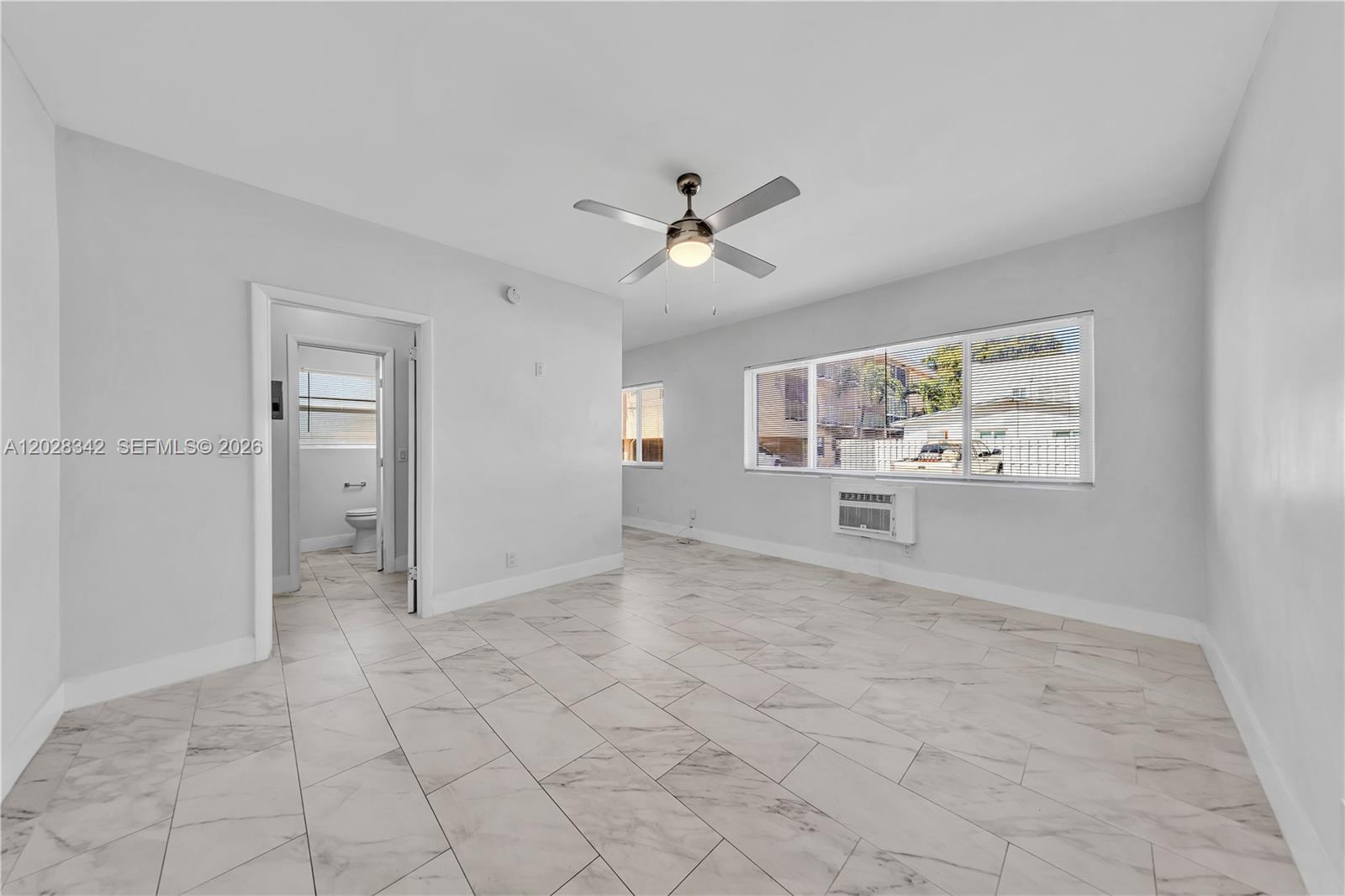 An empty room features light-colored marble-look tile flooring, a ceiling fan, and a window air conditioner — 1839 Funston St # 4, Hollywood FL 33020, HOLLYWOOD, FL