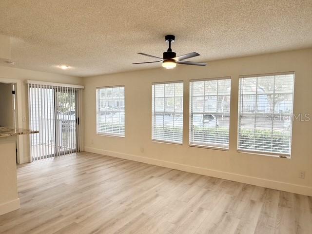 An empty living room features light wood-look flooring, a ceiling fan, and large windows — 11594 WESTWOOD BOULEVARD UNIT 1617, ORLANDO, FL