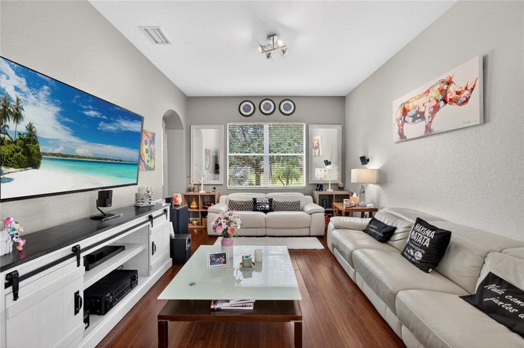 A living room features a large television, white sofas, a glass coffee table, and hardwood floors — VERO BEACH, FL
