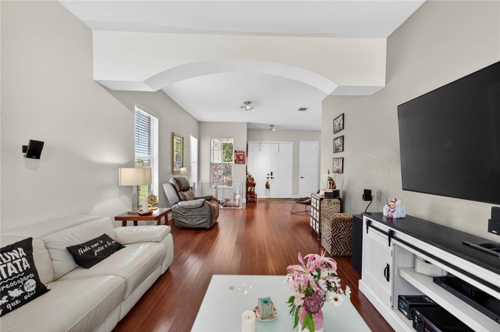 A living room features hardwood floors, a white sofa, a television, and an arched entryway — VERO BEACH, FL