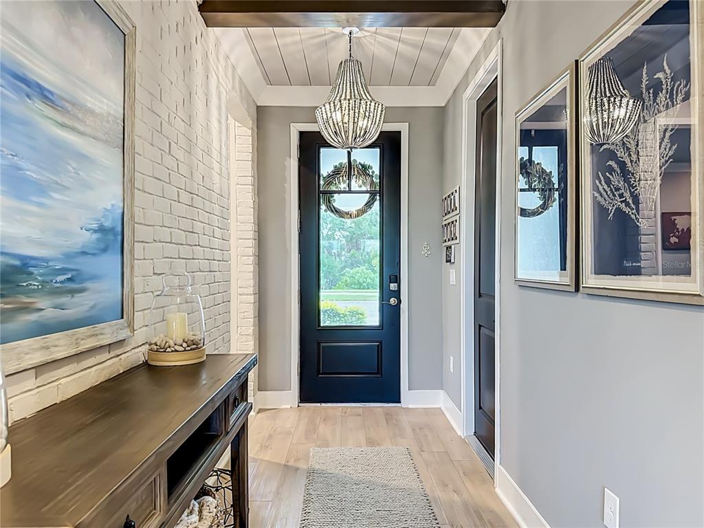 A foyer features a black front door, white brick wall, wood flooring, and a beaded chandelier — 18105 GRAND PROSPERITY DRIVE, VENICE, FL
