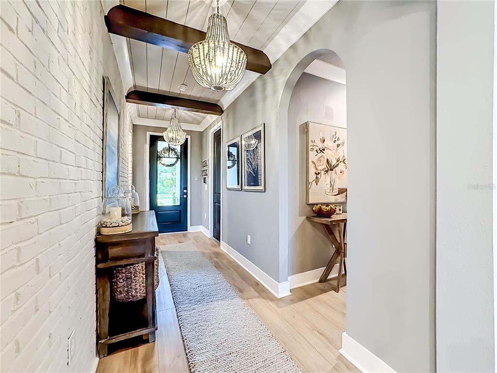 A hallway features a white brick wall, wood-plank ceiling with beams, and two pendant lights — 18105 GRAND PROSPERITY DRIVE, VENICE, FL