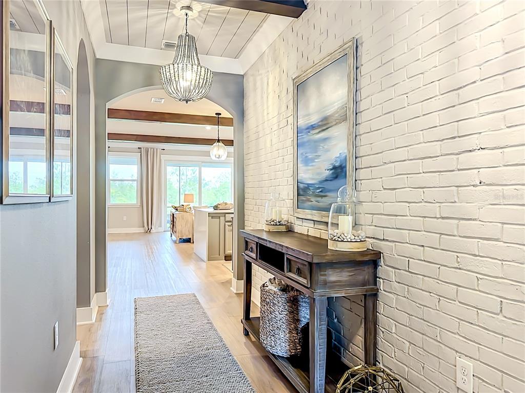A hallway with a white brick wall, wood-look flooring, and a view into a living area — 18105 GRAND PROSPERITY DRIVE, VENICE, FL