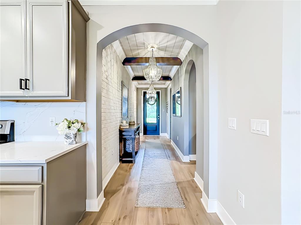 A hallway with a brick wall, wood-plank ceiling, and arched entryway leads to a front door — 18105 GRAND PROSPERITY DRIVE, VENICE, FL