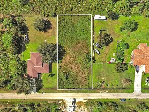 An aerial view shows a vacant, rectangular lot outlined in white between two residential properties — 1413 5TH AVENUE, LEHIGH ACRES, FL