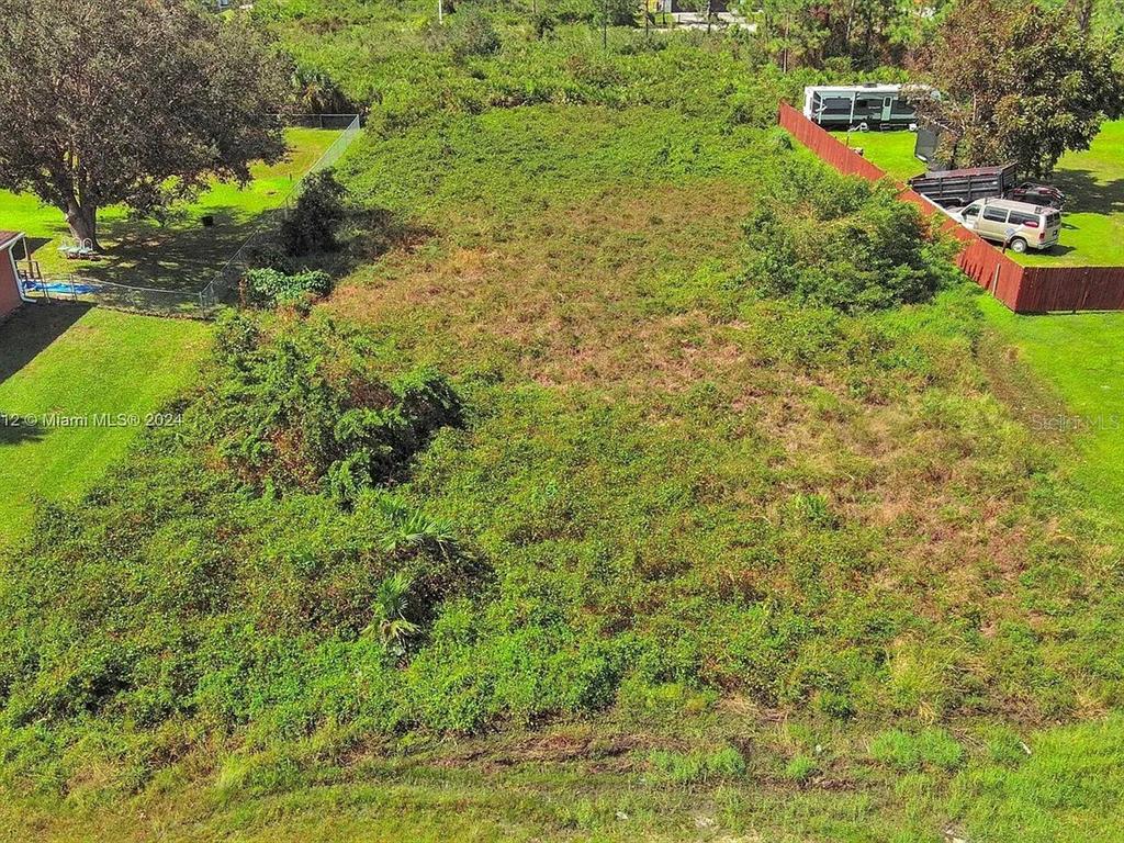 An aerial view shows a vacant, overgrown rectangular lot bordered by fences and trees — 1413 5TH AVENUE, LEHIGH ACRES, FL