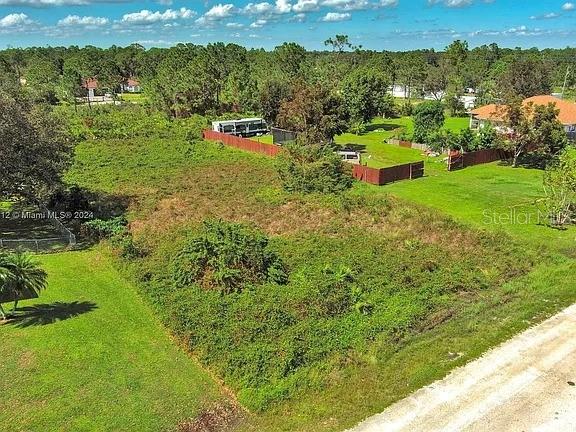 An aerial view shows a vacant, overgrown grassy lot bordered by a fence and trees — 1413 5TH AVENUE, LEHIGH ACRES, FL