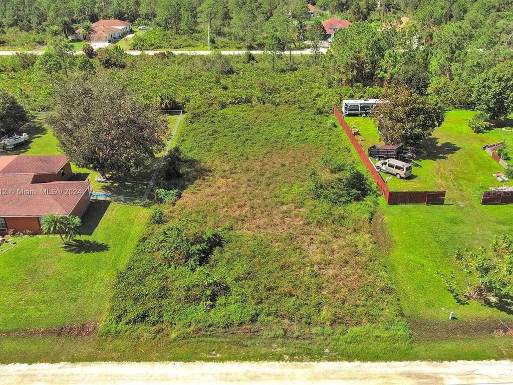 An aerial view shows a vacant, overgrown rectangular lot situated between two residential properties — 1413 5TH AVENUE, LEHIGH ACRES, FL