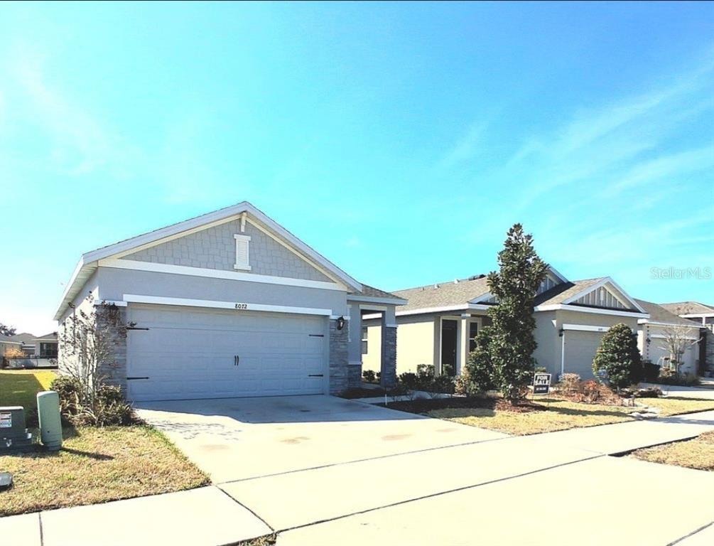 A single-story house with a gray garage, stone accents, and a light-colored driveway — 8072 PENROSE PLACE, WILDWOOD, FL