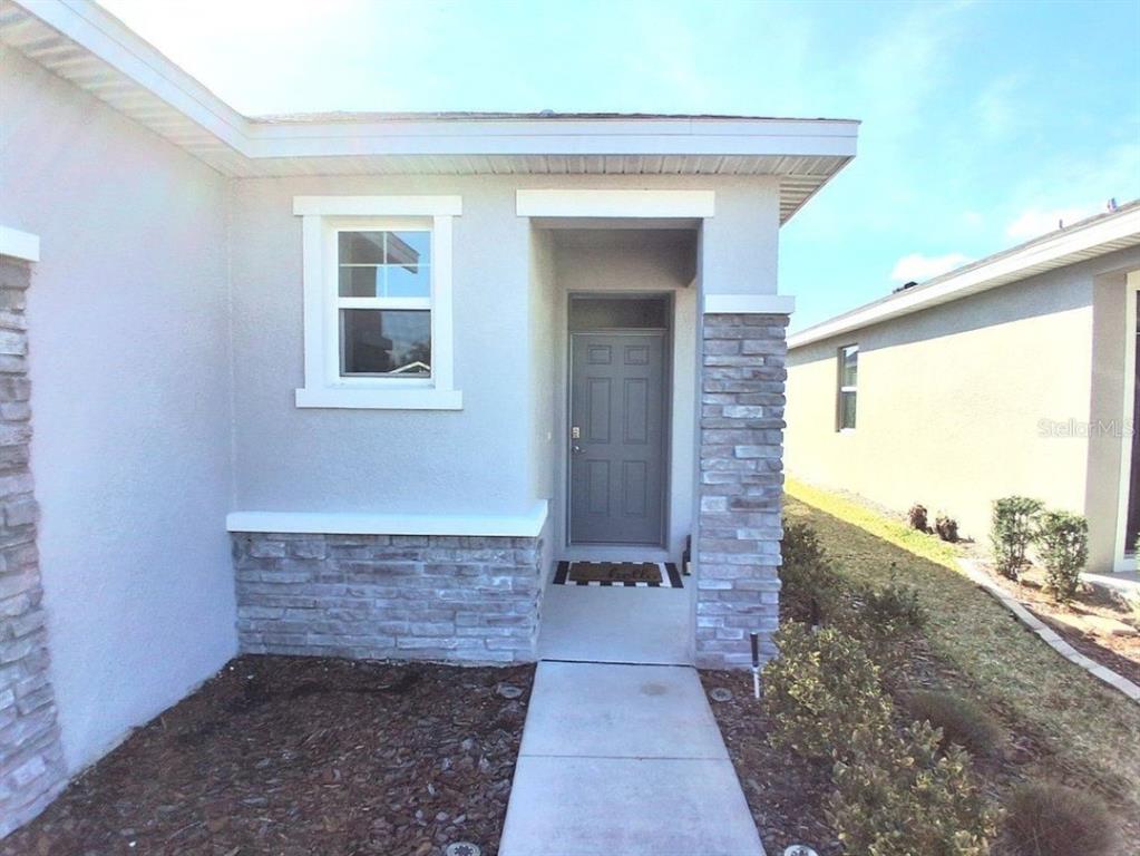 A concrete walkway leads to the front entrance of a house with stone veneer accents — 8072 PENROSE PLACE, WILDWOOD, FL