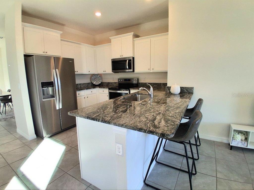 A kitchen features white cabinets, stainless steel appliances, and a dark granite-topped island — 8072 PENROSE PLACE, WILDWOOD, FL