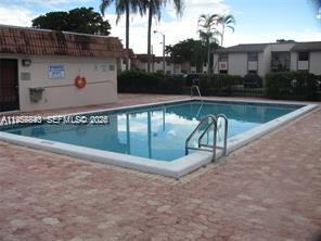 An outdoor swimming pool with a metal ladder sits on a paved patio near buildings — 900 NE 209th Ter # 31, Miami FL 33179, MIAMI, FL