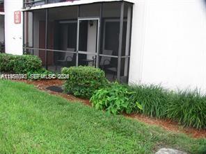 A ground-level screened-in patio with outdoor furniture sits beside a white building and landscaping — 900 NE 209th Ter # 31, Miami FL 33179, MIAMI, FL