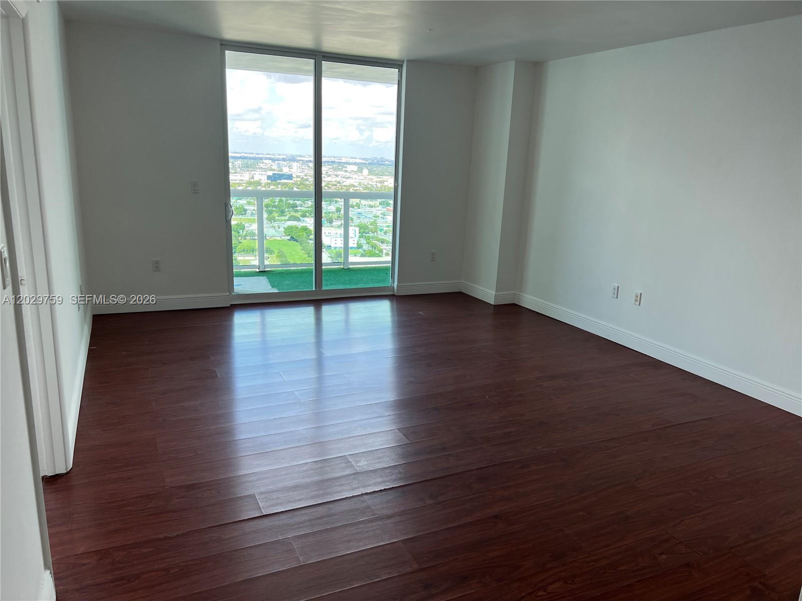 An empty room features dark wood-look flooring, white walls, and a sliding glass door to a balcony — 1800 N Bayshore Dr # 3904, Miami FL 33132, MIAMI, FL