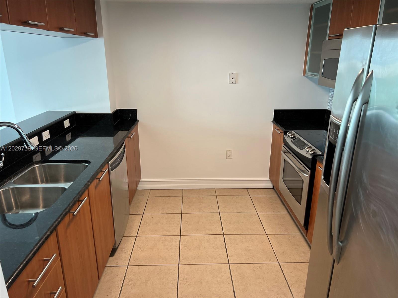 A galley kitchen features wood cabinets, black countertops, stainless steel appliances, and tiled flooring — 1800 N Bayshore Dr # 3904, Miami FL 33132, MIAMI, FL