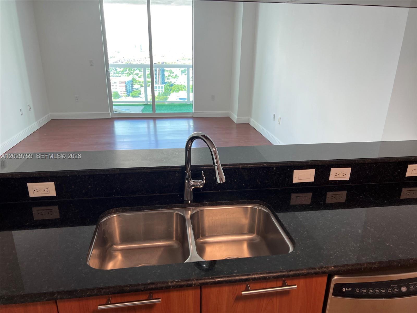 A kitchen sink with a chrome faucet sits in a black countertop overlooking a living area — 1800 N Bayshore Dr # 3904, Miami FL 33132, MIAMI, FL