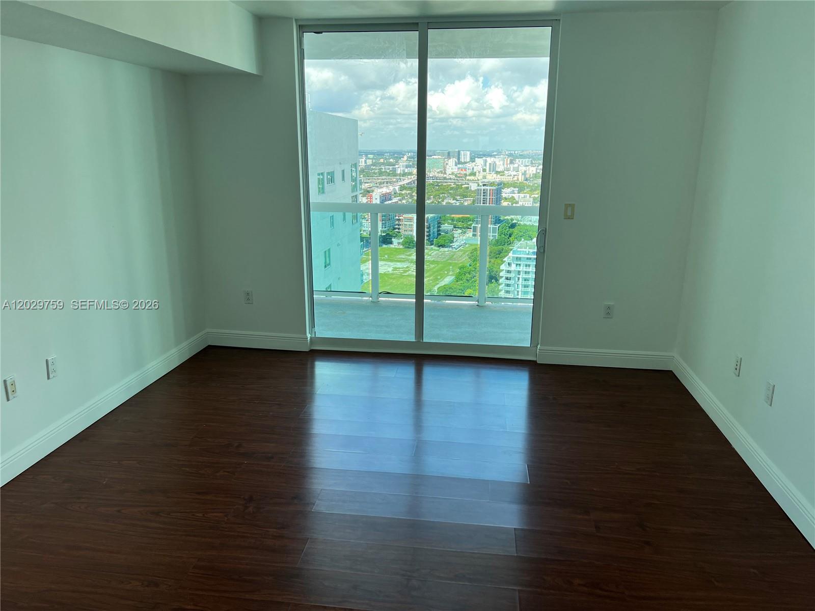 An empty room with dark wood flooring and a sliding glass door leading to a balcony — 1800 N Bayshore Dr # 3904, Miami FL 33132, MIAMI, FL