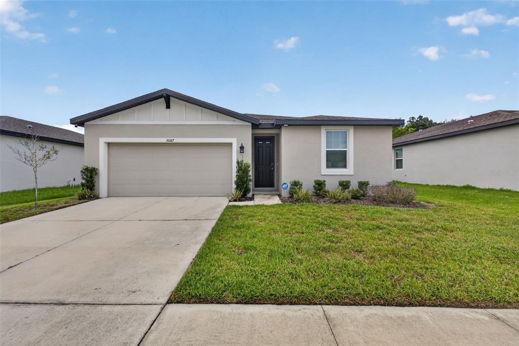 A single-story house with a beige stucco exterior, a two-car garage, and a front lawn — 3087 FORREST PLUM COURT, ZEPHYRHILLS, FL