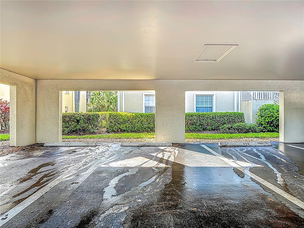 A covered parking area features three numbered concrete parking spaces and a view of landscaping — 25735 LAKE AMELIA WAY UNIT 103, BONITA SPRINGS, FL