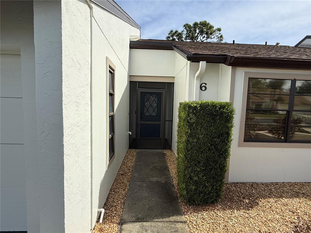 A concrete walkway leads to the front entrance of a white house with a hedge — 1211 CAPRI ISLES BOULEVARD UNIT 6, VENICE, FL