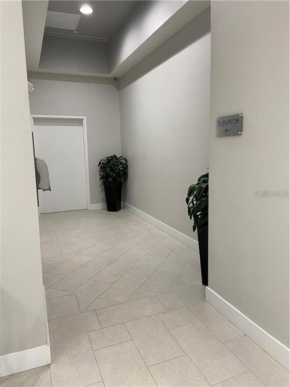 A hallway with light-colored tile flooring, white walls, two potted plants, and an elevator sign — 1500 STATE STREET UNIT 401, SARASOTA, FL