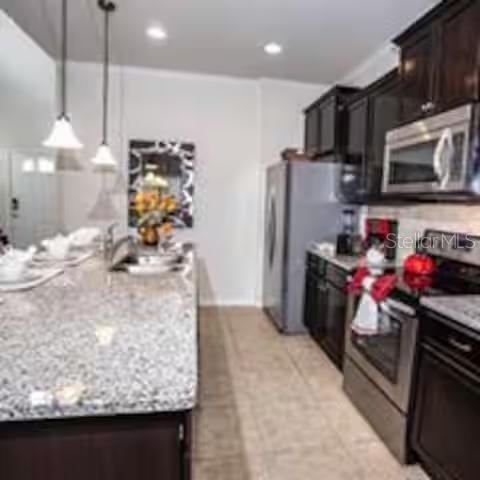 A kitchen features dark wood cabinets, granite countertops, stainless steel appliances, and two pendant lights — 8956 RHODES STREET, KISSIMMEE, FL