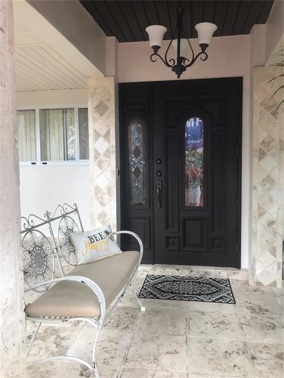 A covered porch features a white metal bench, a dark front door, and tiled flooring — 14821 PALMETTO PALM AVENUE, MIAMI LAKES, FL