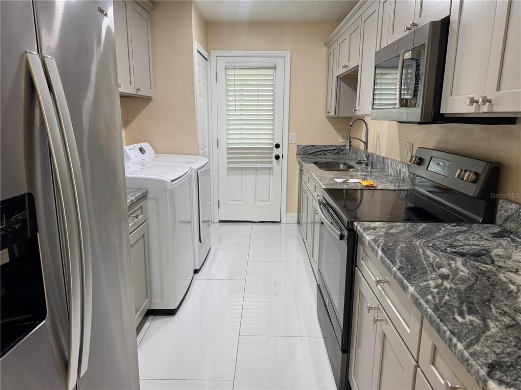 A laundry room featuring white appliances, gray cabinets, granite countertops, and white tile flooring — 725 NORTHLAKE BOULEVARD UNIT 18, ALTAMONTE SPRINGS, FL