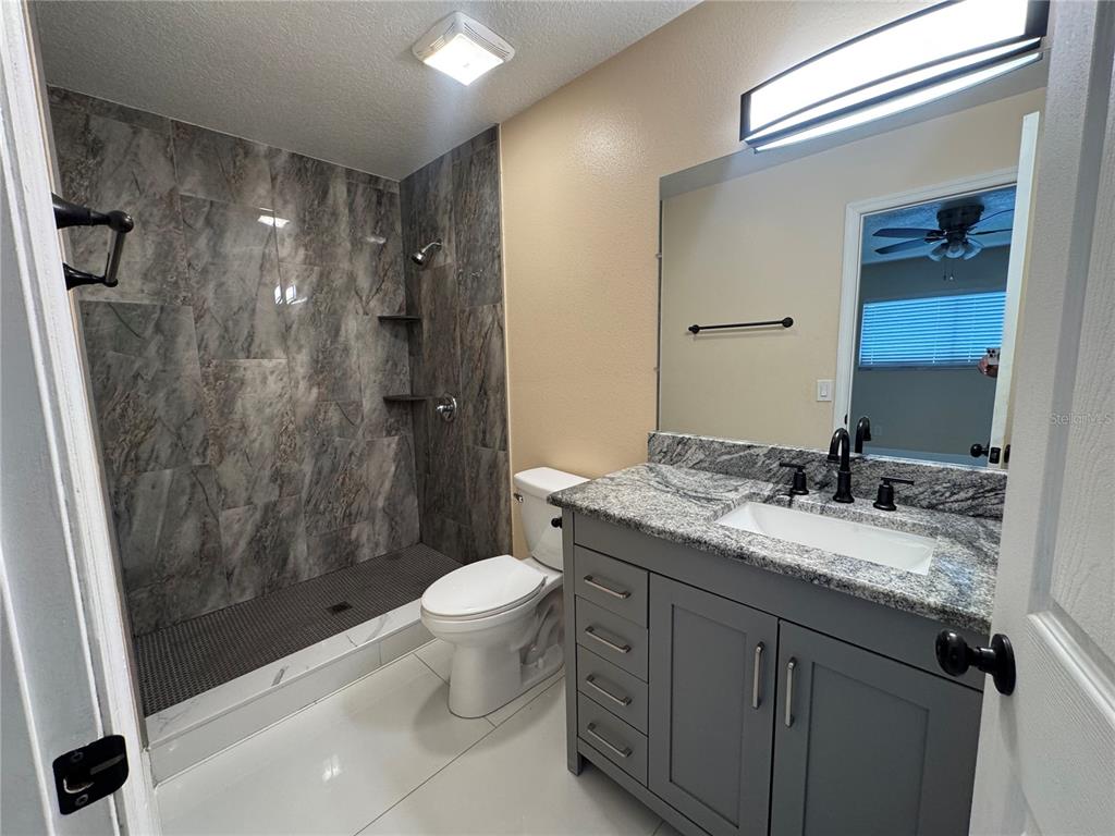 A bathroom features a gray vanity with a granite countertop, a toilet, and a tiled shower — 725 NORTHLAKE BOULEVARD UNIT 18, ALTAMONTE SPRINGS, FL