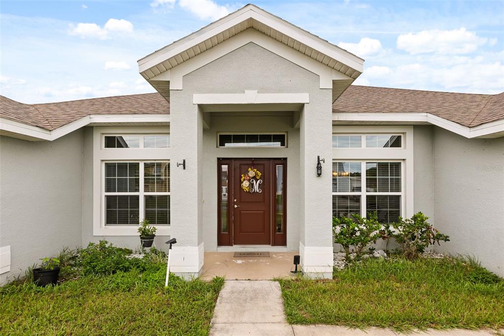 The exterior of a single-story house features a covered entryway with a brown front door — 1234 NELSON PARK CT, POINCIANA, FL