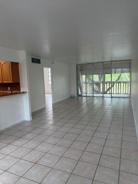 An empty room with light-colored tile flooring, a kitchen area, and a large sliding glass door — 7031 Environ Blvd # 221, Lauderhill FL 33319, LAUDERHILL, FL
