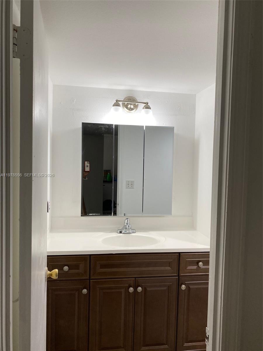 A bathroom features a dark wood vanity, white countertop, and a three-panel medicine cabinet — 7031 Environ Blvd # 221, Lauderhill FL 33319, LAUDERHILL, FL
