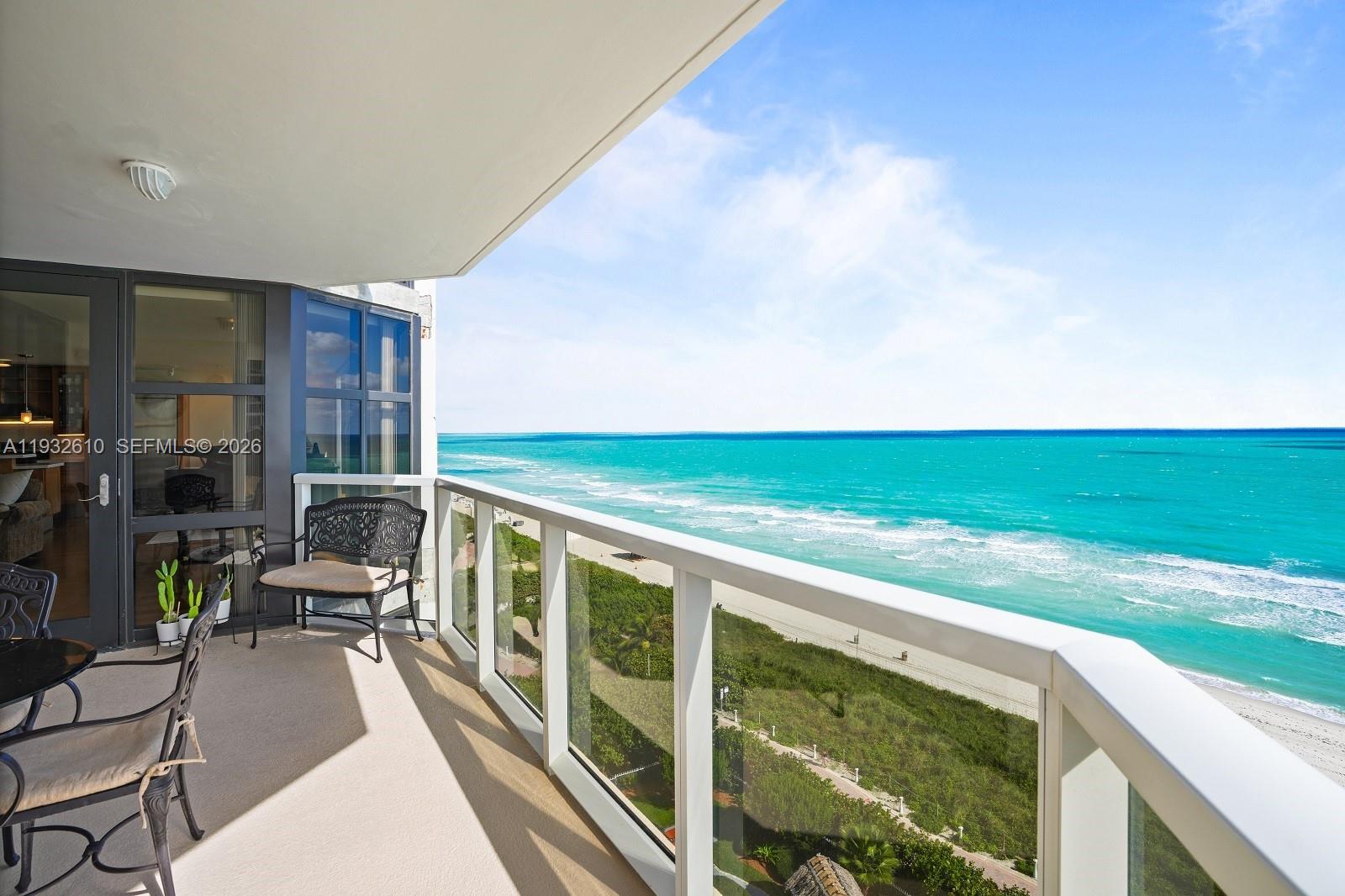 A balcony with outdoor furniture overlooks a sandy beach and the turquoise ocean — 6423 Collins Ave # 1005, Miami Beach FL 33141, MIAMI BEACH, FL