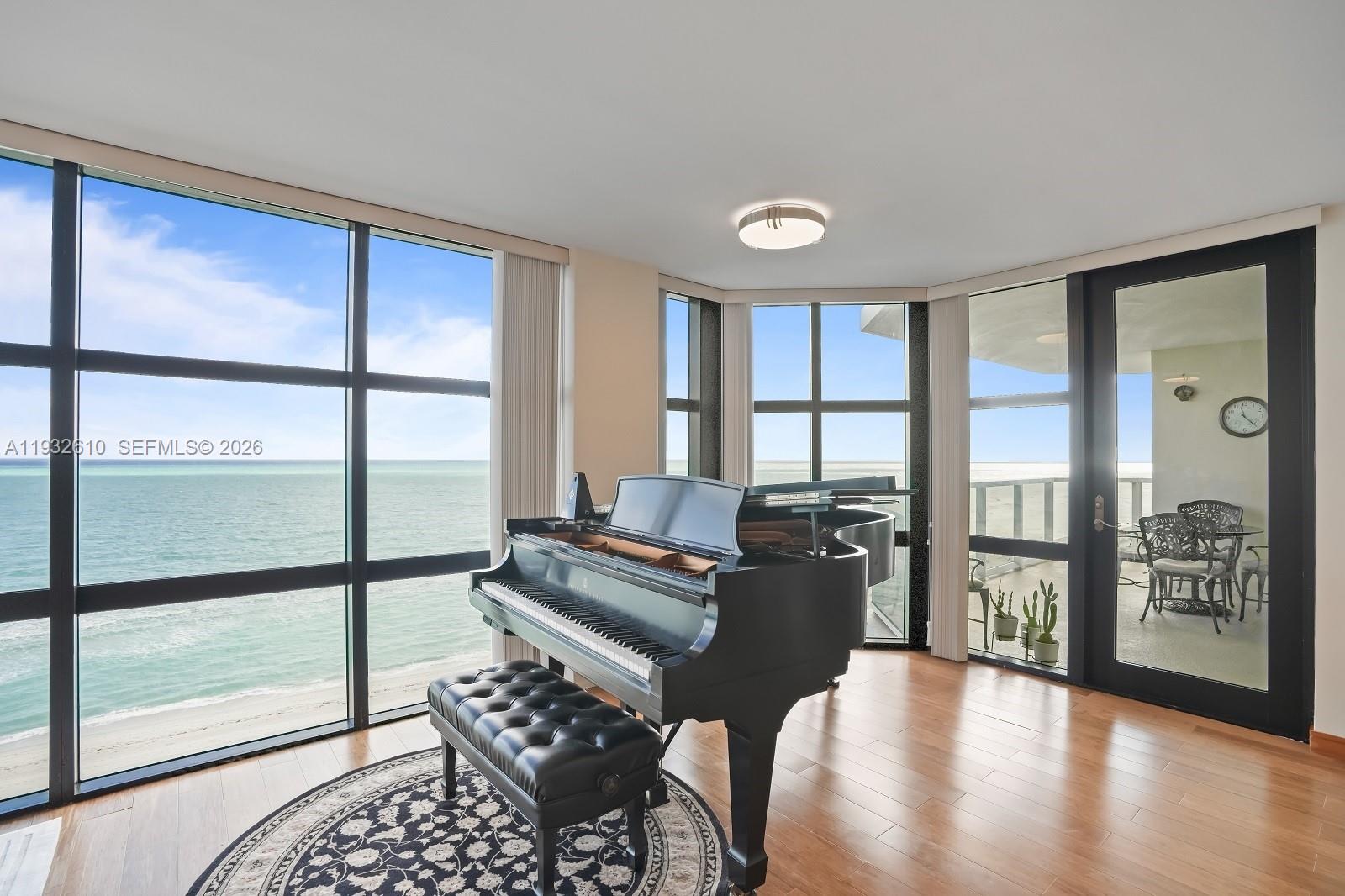 A grand piano sits on a circular rug in a room with floor-to-ceiling ocean views — 6423 Collins Ave # 1005, Miami Beach FL 33141, MIAMI BEACH, FL