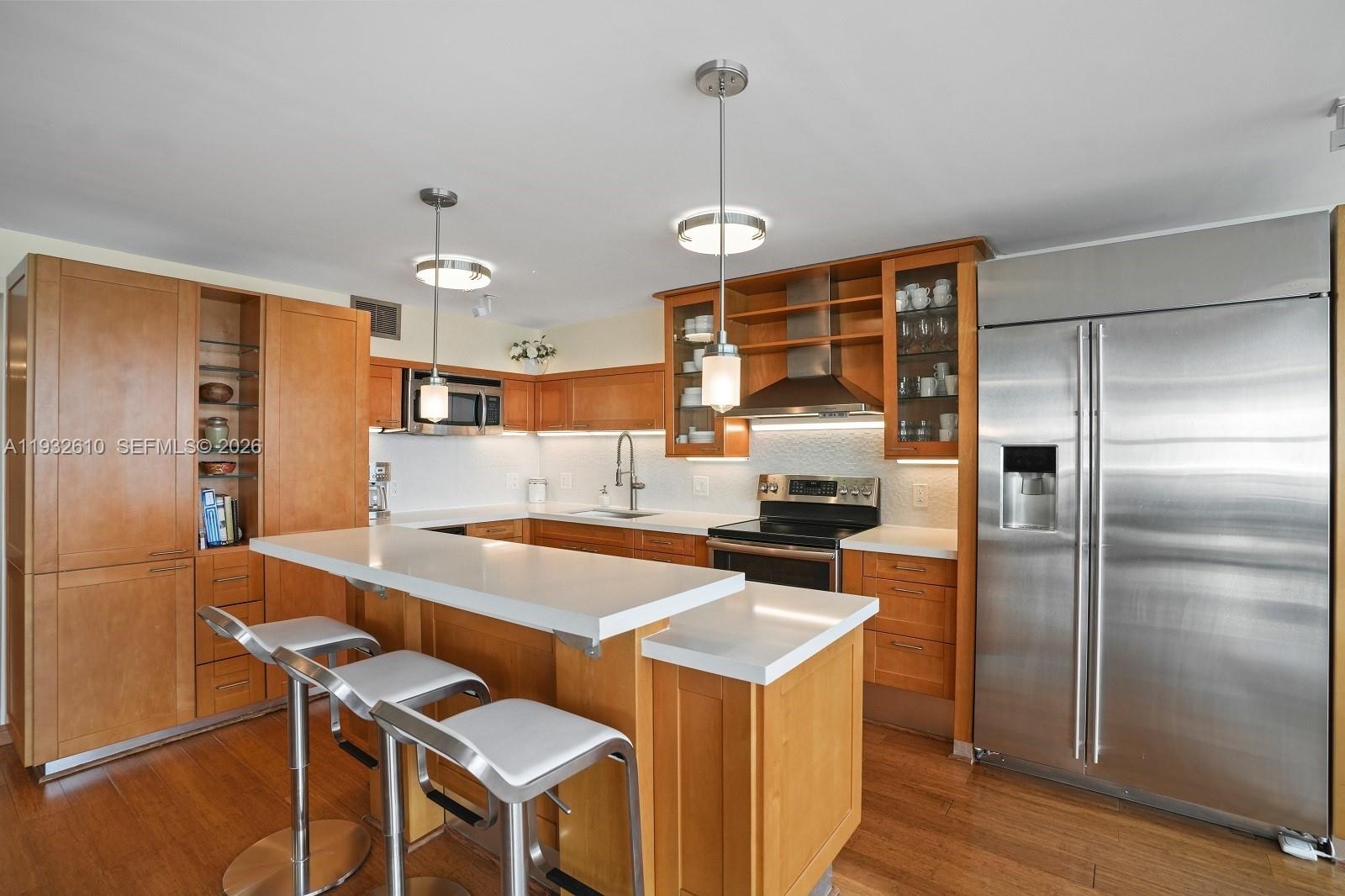 A kitchen features light wood cabinets, a white countertop island, and stainless steel appliances — 6423 Collins Ave # 1005, Miami Beach FL 33141, MIAMI BEACH, FL