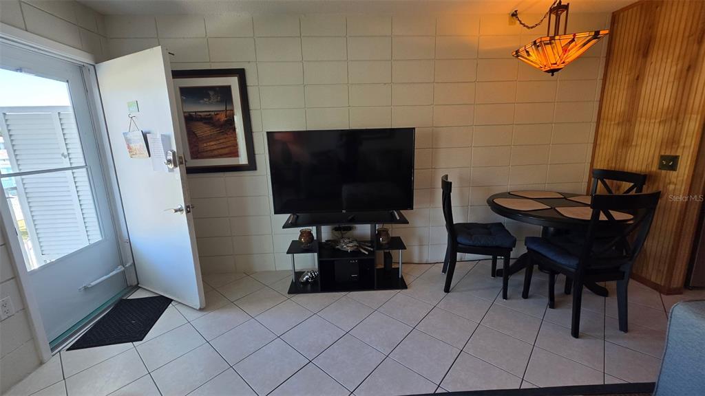 A room with a white block wall, a television on a stand, and a dining set — 541 S PENINSULA AVENUE UNIT A21, NEW SMYRNA BEACH, FL