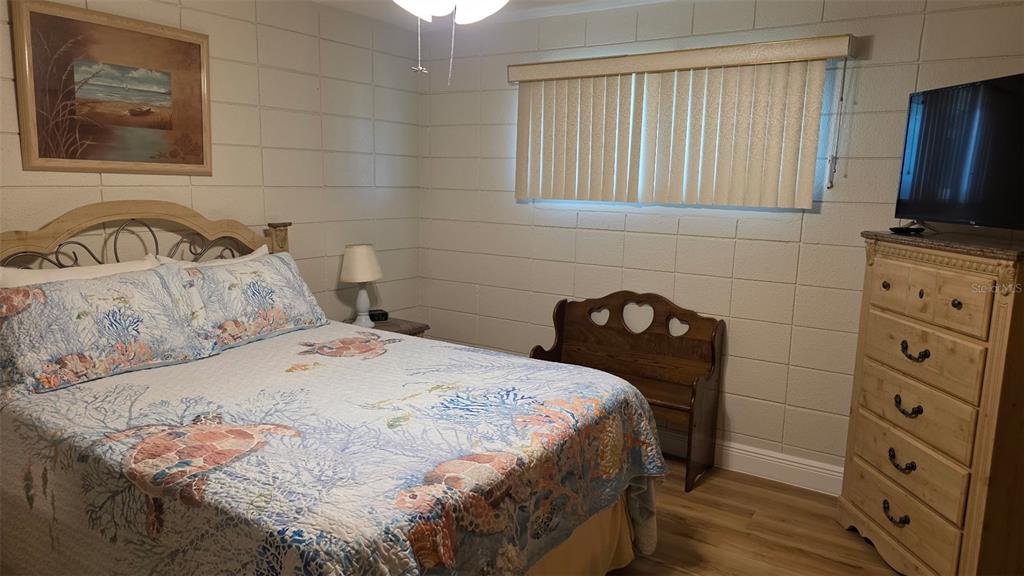A bedroom features a bed with a coastal quilt, cinder block walls, and a wooden dresser — 541 S PENINSULA AVENUE UNIT A21, NEW SMYRNA BEACH, FL