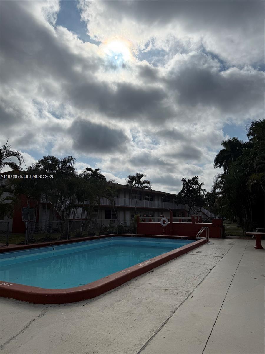 An outdoor swimming pool sits in front of a multi-story apartment building under a cloudy sky — 2915 Plunkett St # 12A, Hollywood FL 33020, HOLLYWOOD, FL