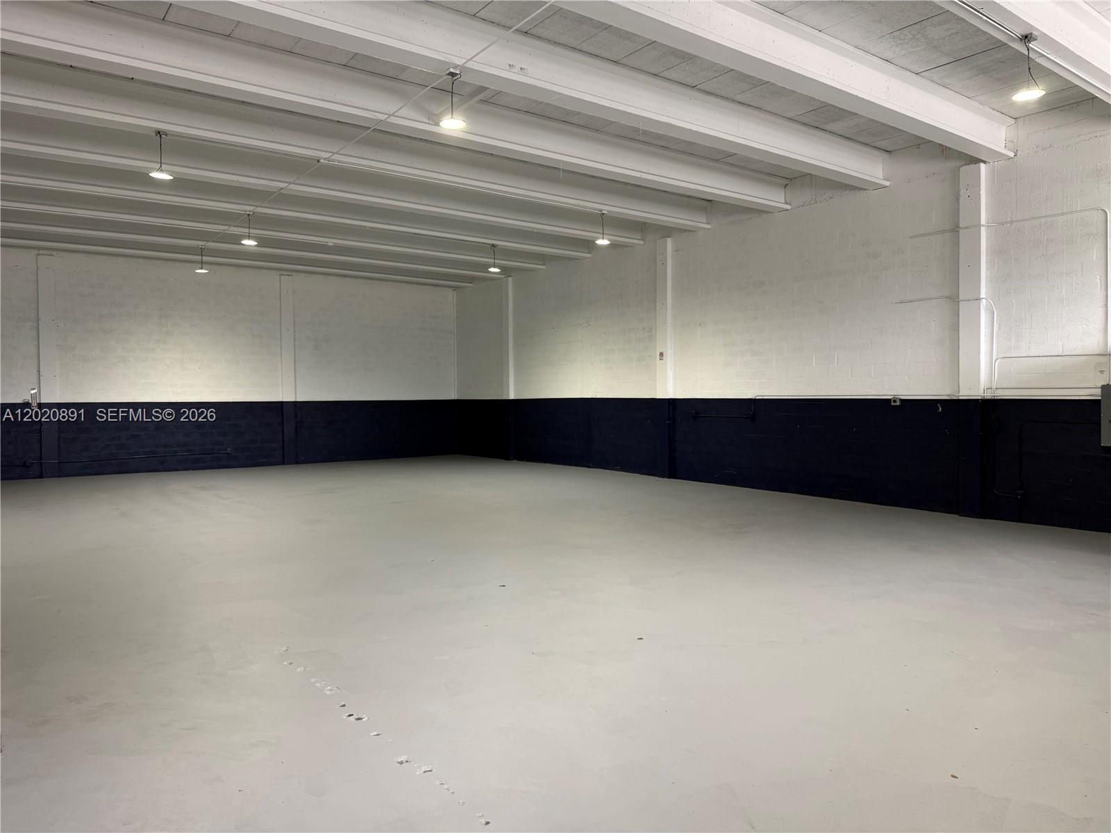 An empty industrial warehouse space features white walls, a dark wainscot, and exposed ceiling beams — 3911 NW 25 ST, Miami FL 33142, MIAMI, FL