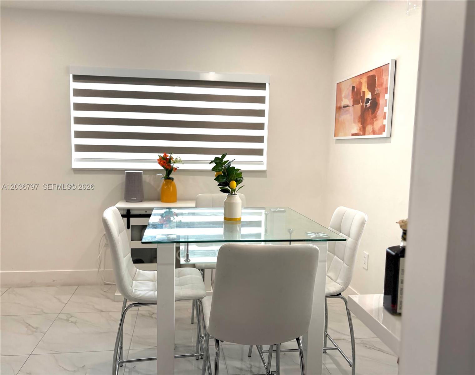 A dining room features a glass-topped table, four white chairs, and a window with blinds — 6515 SW 20th Ct, Miramar FL 33023, MIRAMAR, FL