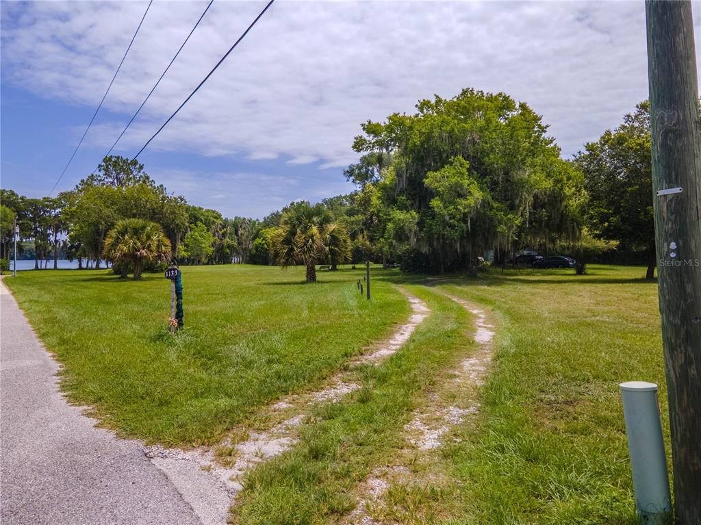 A grassy lot features a dirt driveway, scattered trees, and a view of a lake — 1133 BELLA LAGO COVE, WINTER PARK, FL