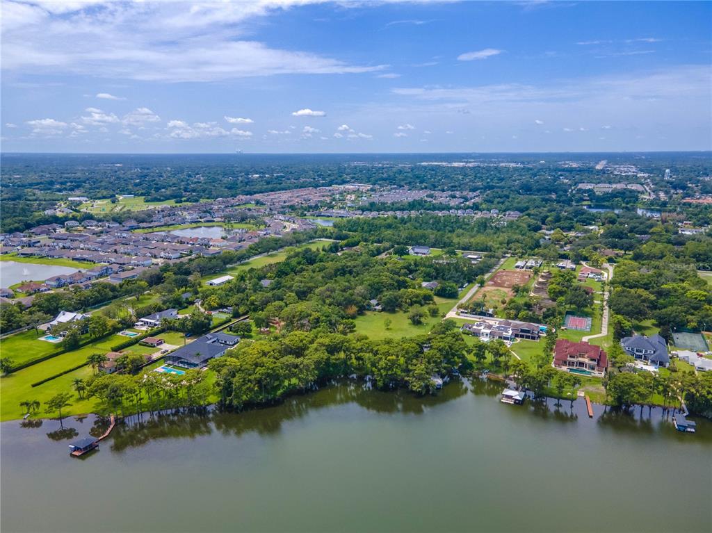 An aerial view shows several large waterfront homes surrounded by trees and a suburban neighborhood — 1133 BELLA LAGO COVE, WINTER PARK, FL