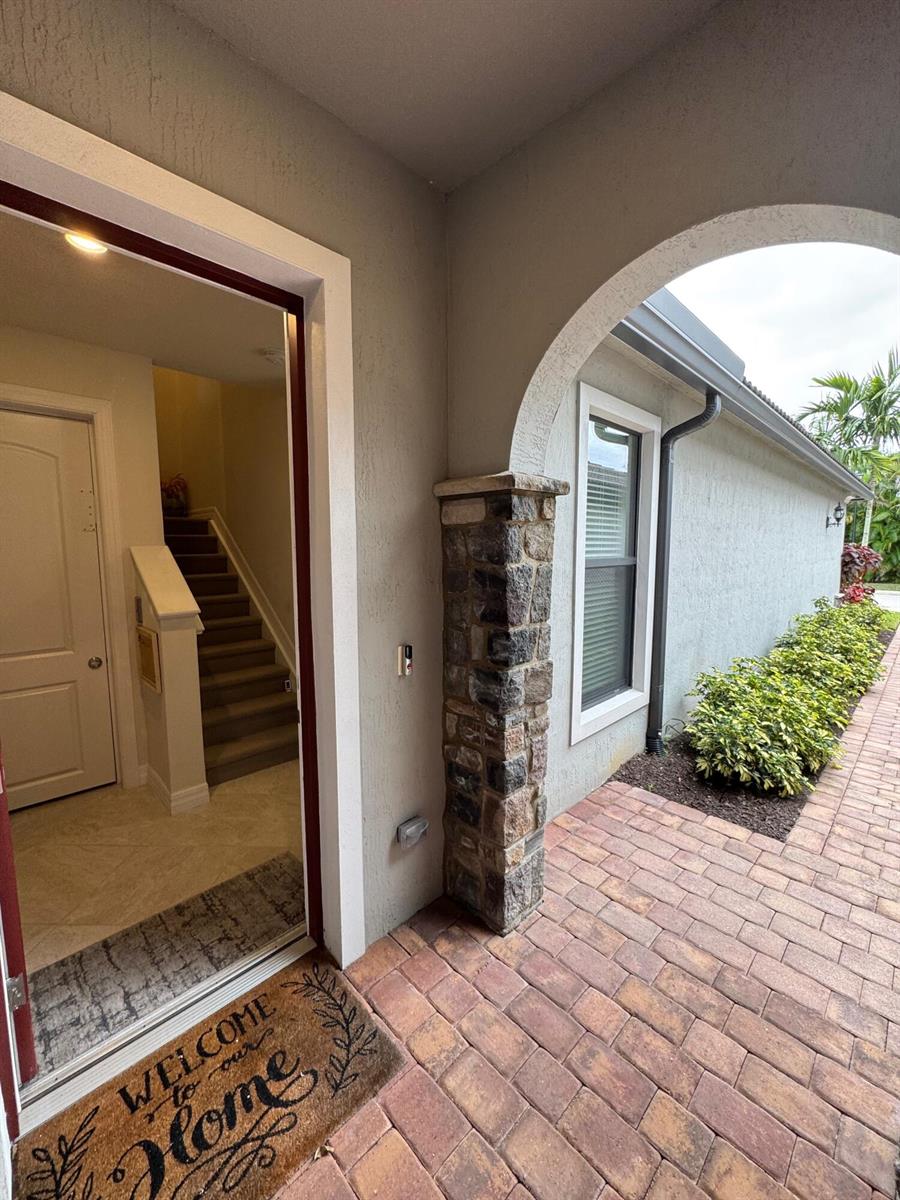 A stone-accented arched entryway leads into a home with a staircase visible inside — 21872 Canadensis Circle # 202, Boca Raton FL 33428, BOCA RATON, FL
