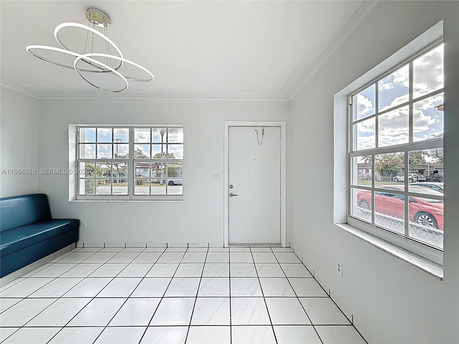 A bright room features white tiled floors, a modern light fixture, and two grid-paneled windows — 6819 SW 25th St, Miami FL 33155, MIAMI, FL