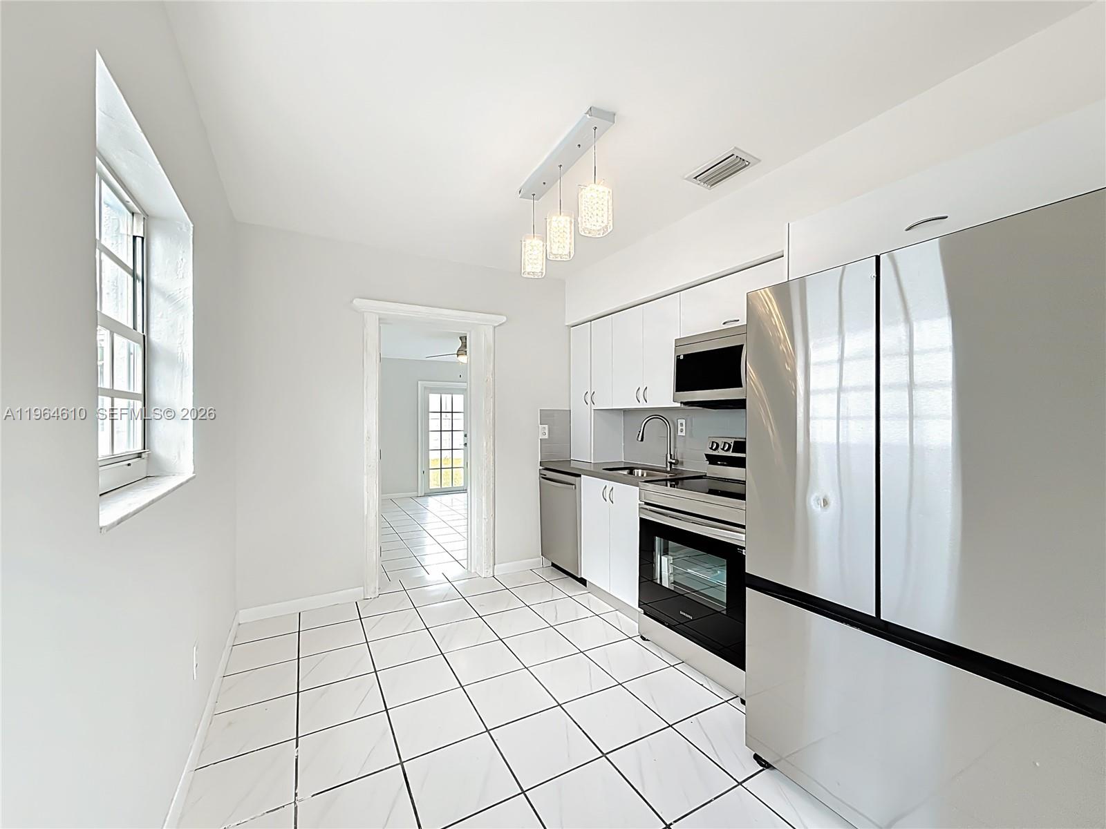 A kitchen features white cabinets, stainless steel appliances, and white tile flooring — 6819 SW 25th St, Miami FL 33155, MIAMI, FL