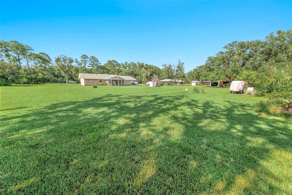 A large grassy backyard features a single-story house with a screened porch and mature trees — 2041 HALIFAX DRIVE, PORT ORANGE, FL