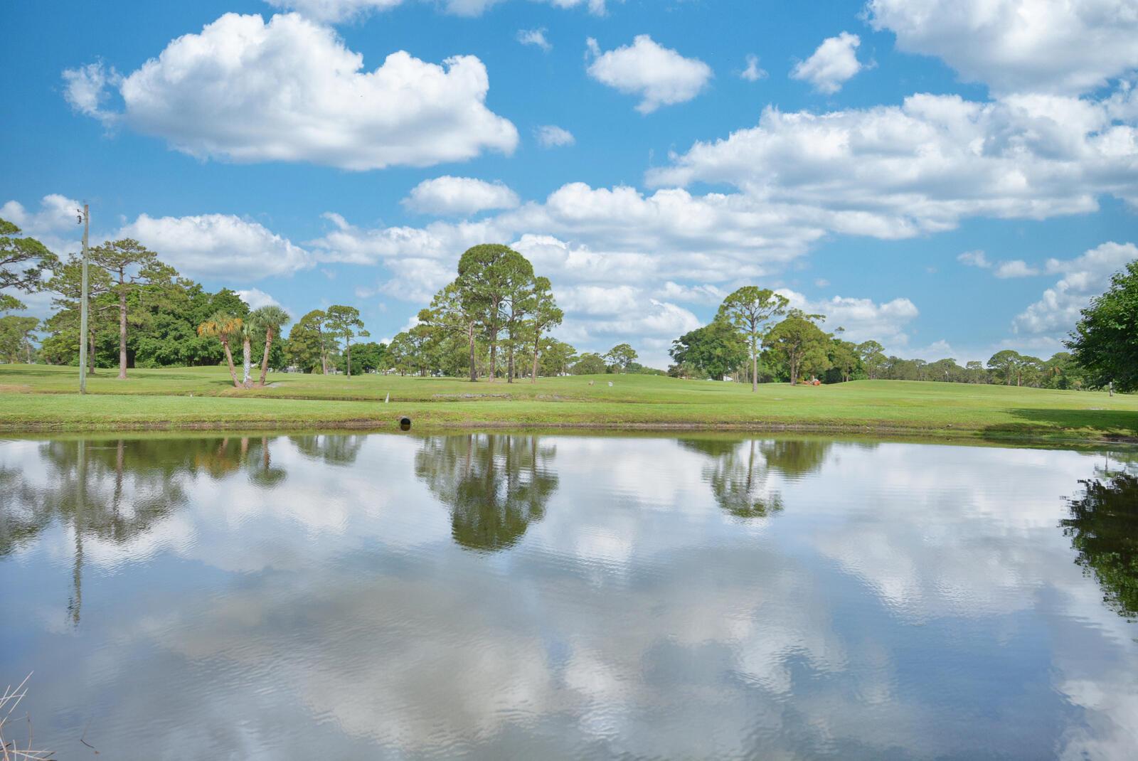 A calm pond reflects the blue sky and surrounding trees on a sunny golf course — 1225 NW 21st Street # 2105, Stuart FL 34994, STUART, FL