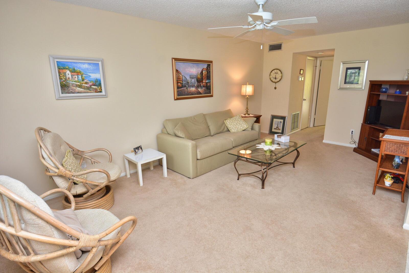 A living room features beige carpet, a tan sofa, two wicker chairs, and a glass-topped table — 1225 NW 21st Street # 2105, Stuart FL 34994, STUART, FL