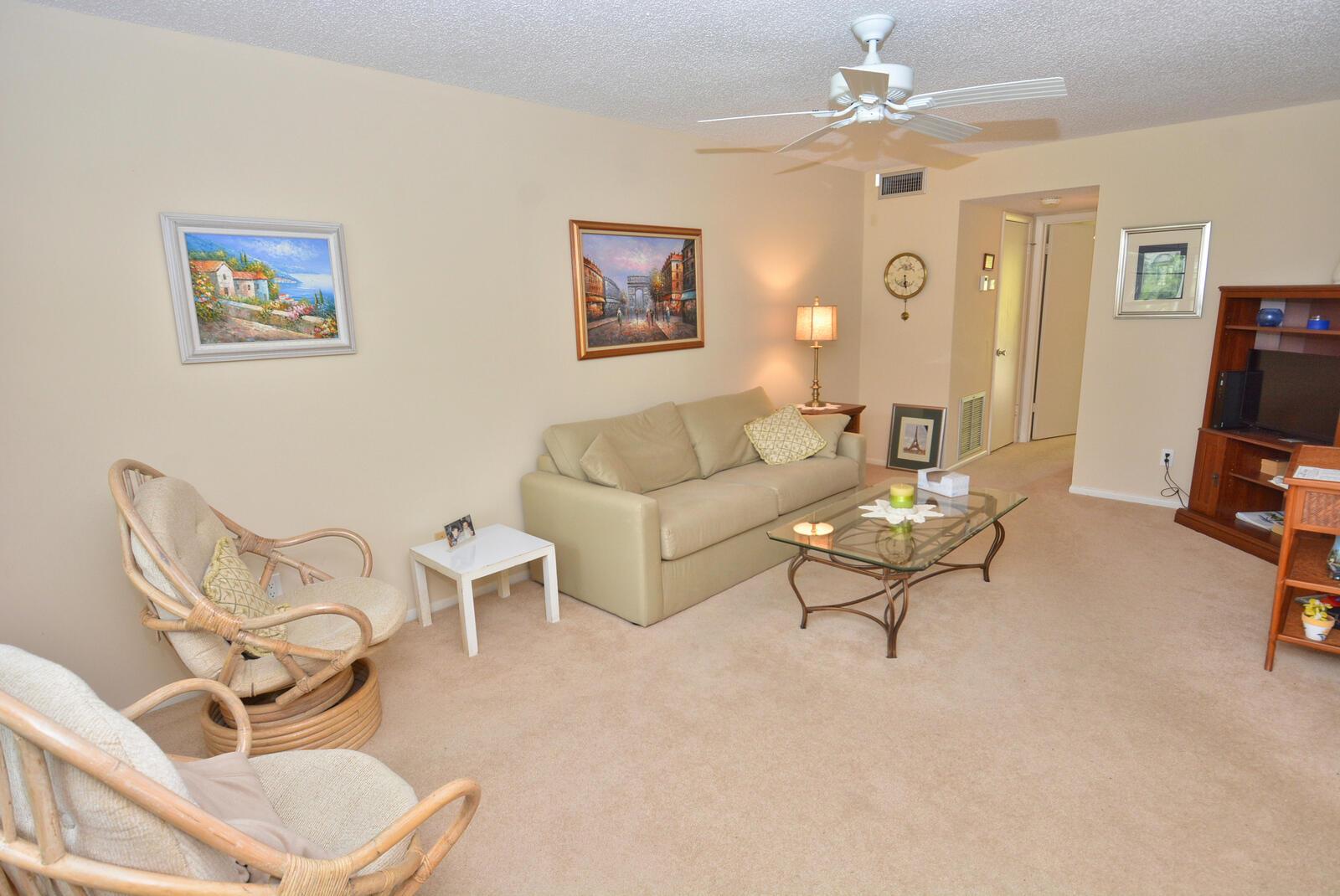 A living room features beige carpet, a tan sofa, two wicker chairs, and a ceiling fan — 1225 NW 21st Street # 2105, Stuart FL 34994, STUART, FL